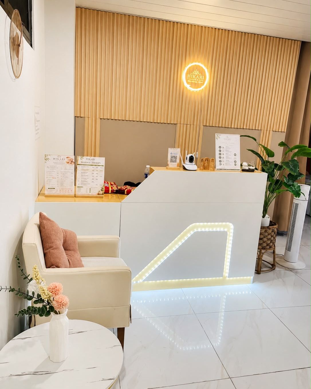 Reception desk at Hikari Massage and Spa with the lit Hikari sign on a wood slat wall and service menus on the counter