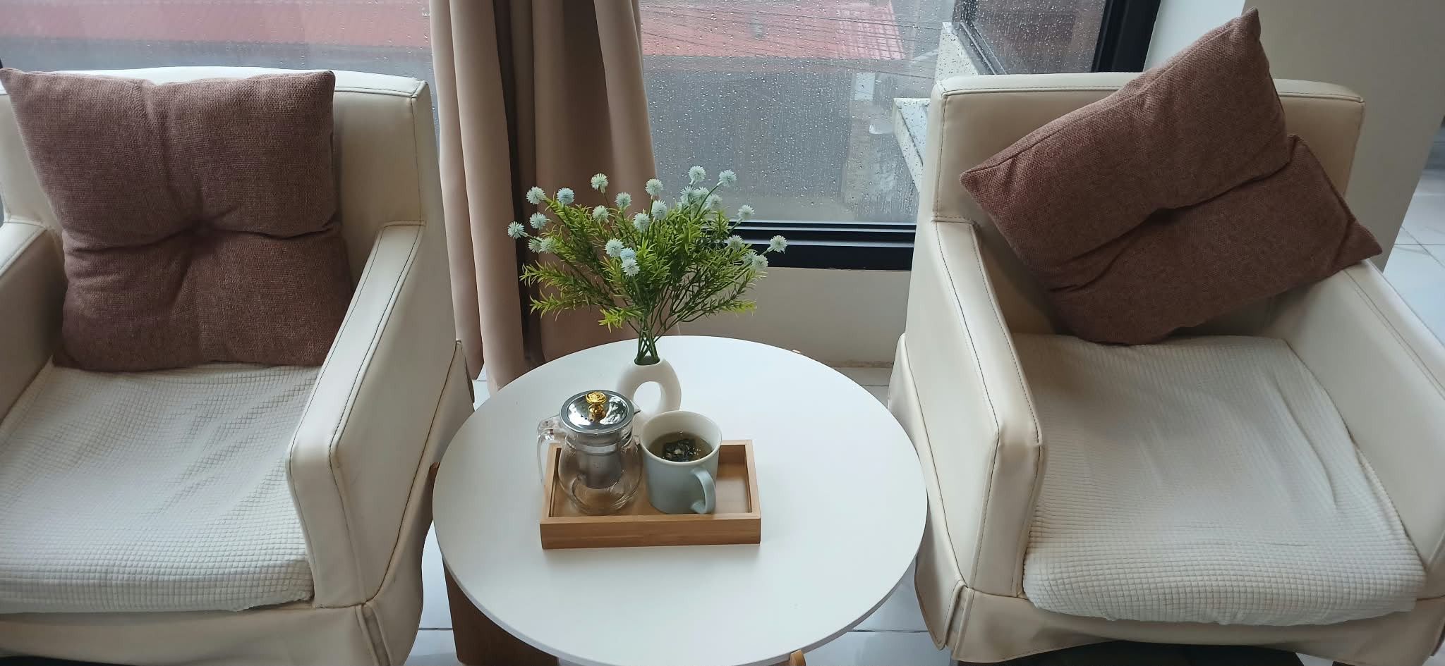 Two cream armchairs and a round table with herbal tea by the window in the lounge at Hikari Massage and Spa